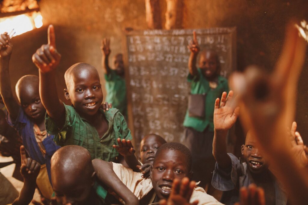 Smiling boys raising their hands in a classroom in Uganda